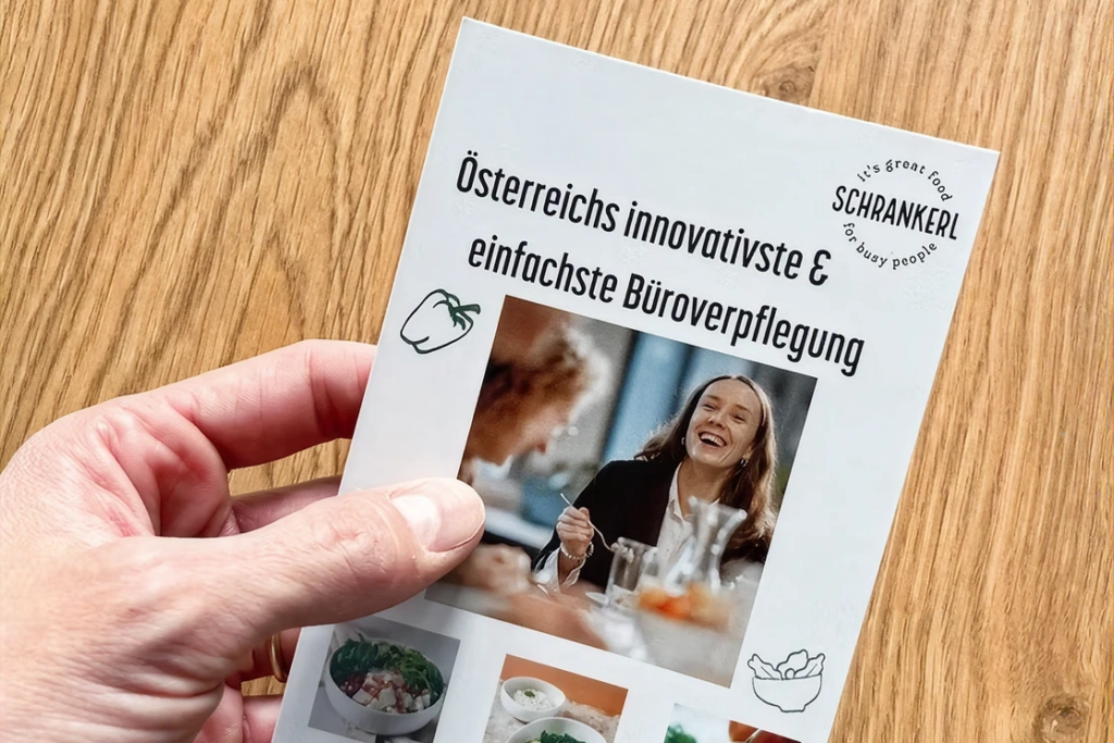 Eine Hand hält einen Prospekt von Schrankerl für moderne Mitarbeiterverpflegung im Büro.