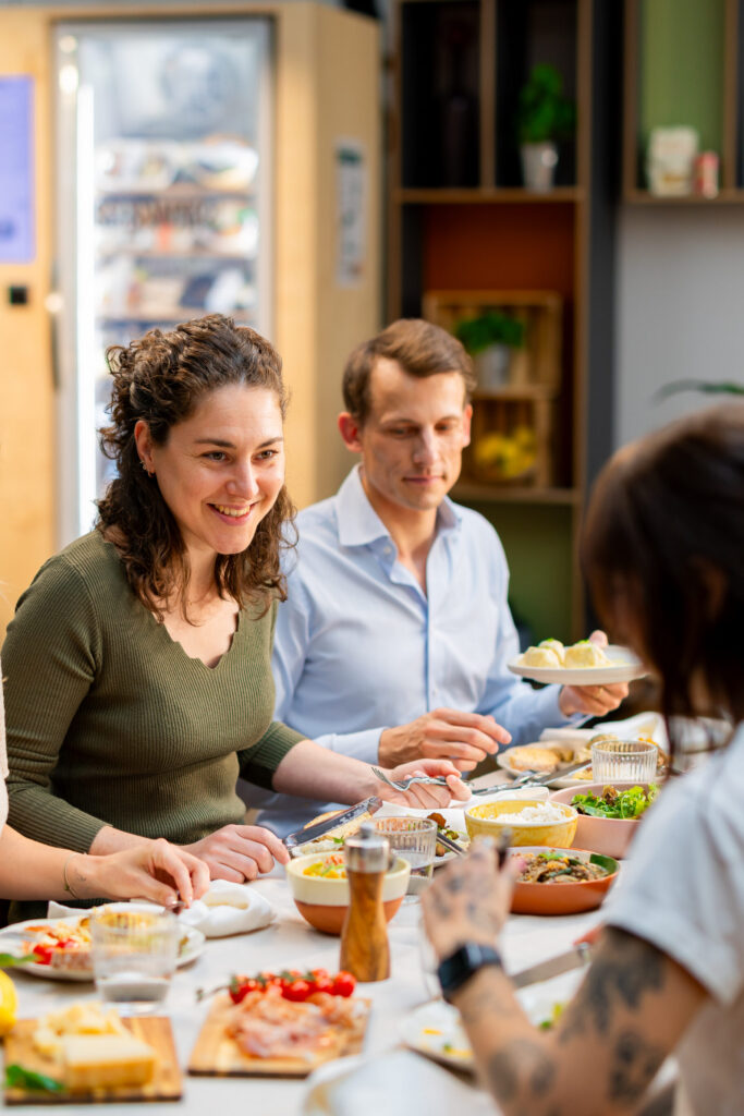 Kolleginnen und Kollegen genießen gemeinsam frisches Essen bei der gesunden Mitarbeiterverpflegung im Büro.