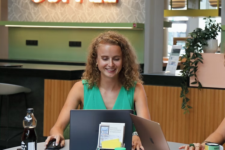Eine lächelnde Frau arbeitet am Laptop im Büro mit moderner Mitarbeiterverpflegung.