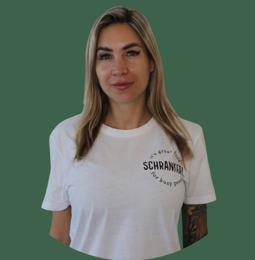 Blonde Frau im weißen T-Shirt des Anbieters Schrankerl für moderne Mitarbeiterverpflegung vor grünem Hintergrund.