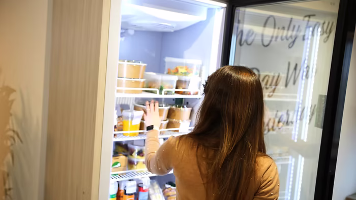 Eine Frau greift nach frischem Essen aus dem Schrankerl Kühlschrank zur Mitarbeiterverpflegung.