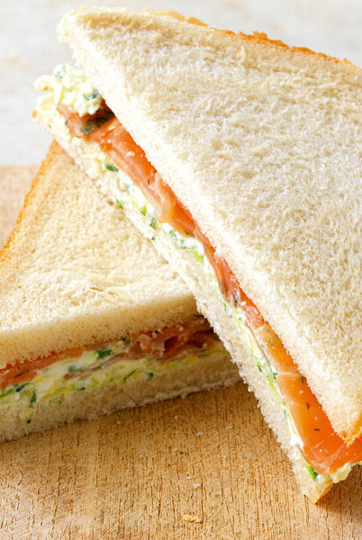 Frisch zubereitetes Lachs-Sandwich mit Kräutercreme als gesunde Mitarbeiterverpflegung auf einem Holzbrett.