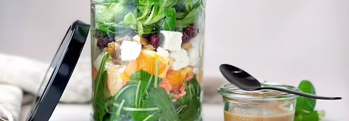 Frischer Schichtsalat im Glas als gesunde Mitarbeiterverpflegung mit Feta, Nüssen und Dressing.