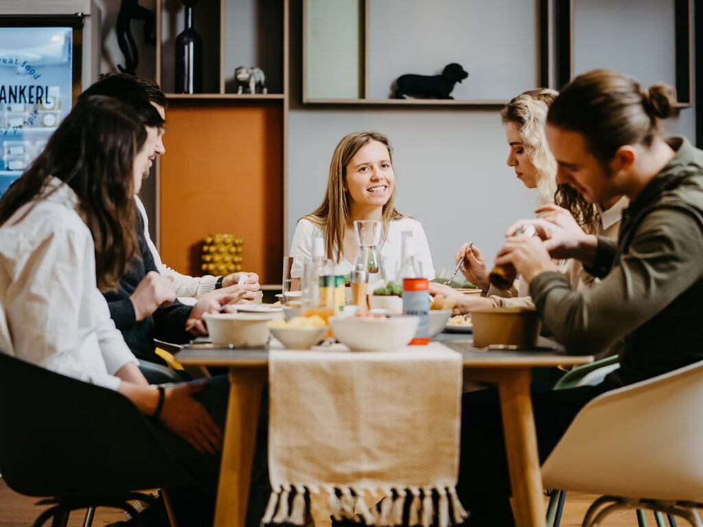 Kolleginnen und Kollegen genießen frische Mitarbeiterverpflegung aus Lunchboxen gemeinsam im Büro.