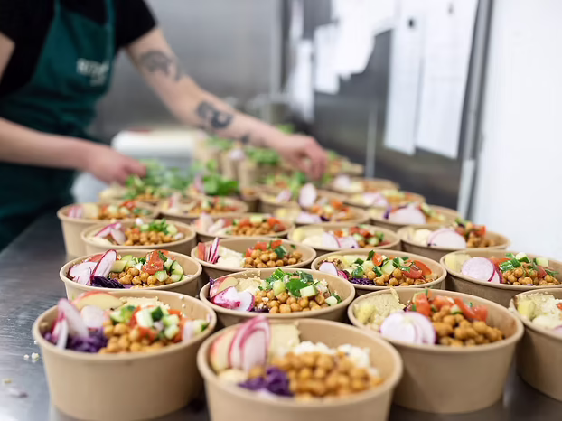 Küchenkraft bereitet viele frische Bowls mit Kichererbsen und Gemüse für die Mitarbeiterverpflegung zu.