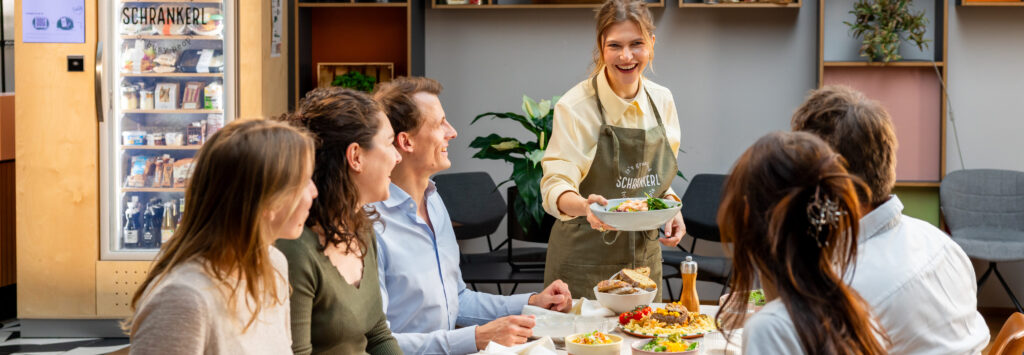 Eine lächelnde Frau serviert eine gesunde Mahlzeit für die Schrankerl Mitarbeiterverpflegung im Büro.