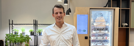 Ein lächelnder Mann steht vor einem Schrankerl-Kühlschrank für moderne Mitarbeiterverpflegung im Büro.